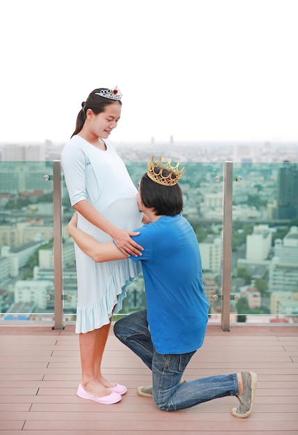 Hombre asiático con corona y arrodillarse con besos vientre de mujer embarazada en el techo de buil