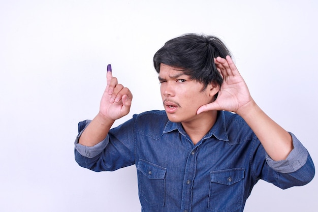 Hombre asiático curioso mostrando un gesto de escucha mientras muestra el dedo meñique con parches de tinta azul Indo