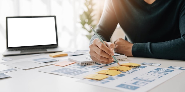Hombre asiático disfrutando en el diseño de papeleo de medios con otros proveedores de oficina sobre notas adhesivas en la pizarra concepto de desarrollo digital creativo
