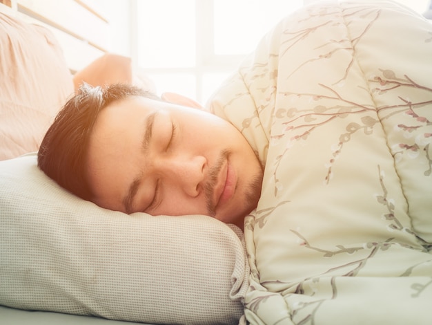 Hombre asiático durmiendo en la luz de la mañana con la cara feliz.