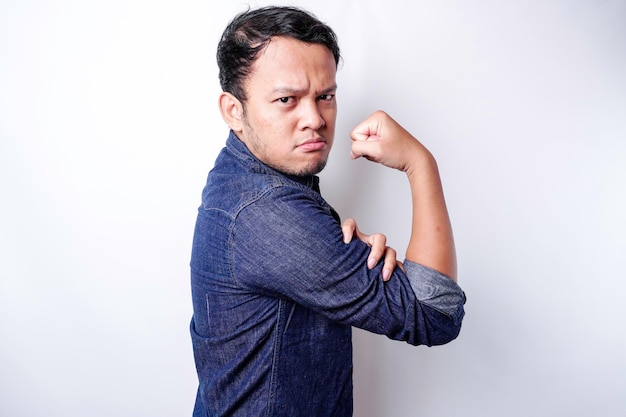 Hombre asiático emocionado con una camisa azul que muestra un gesto fuerte levantando los brazos y los músculos sonriendo con orgullo