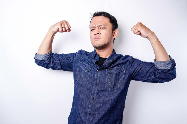 Hombre asiático emocionado con una camisa azul que muestra un gesto fuerte levantando los brazos y los músculos sonriendo con orgullo