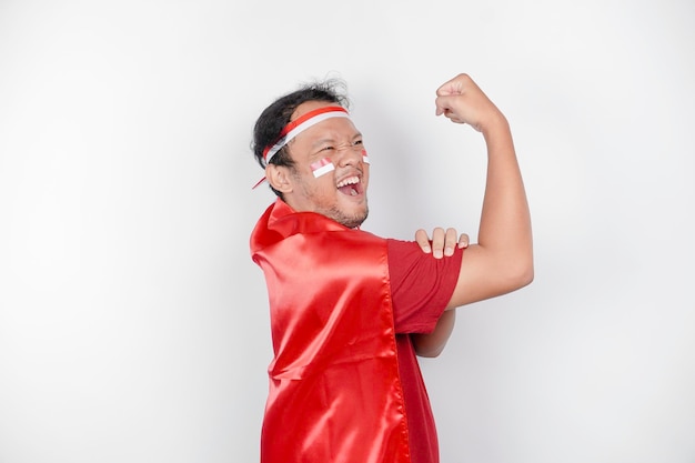 Hombre asiático emocionado con una capa de bandera roja y una cinta para la cabeza mostrando un gesto fuerte levantando sus brazos y músculos sonriendo orgullosamente concepto del día de la independencia de Indonesia39