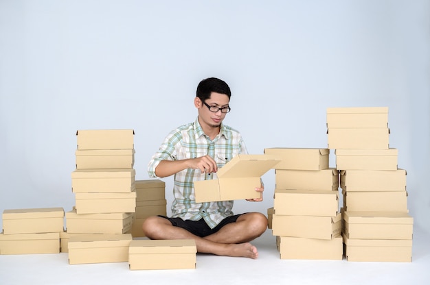 Hombre asiático empacando productos para vender en línea entre muchas cajas con paquetes. Concepto de inicio independiente y oficina en casa de negocios en línea.