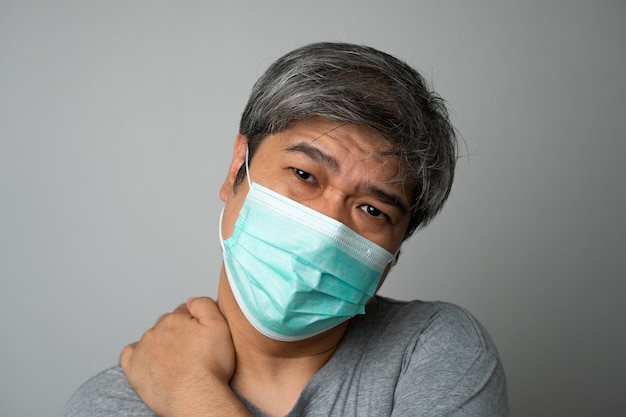 Hombre asiático enfermo con una mascarilla médica y dolor y estrés en el hombro. Concepto de protección frente a coronavirus pandémico y enfermedad respiratoria.