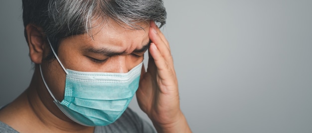 Hombre asiático enfermo con una mascarilla médica y tome una mano para sostener el dolor de cabeza en la cabeza. Concepto de protección frente a coronavirus pandémico y enfermedad respiratoria.