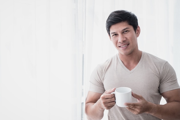 El hombre asiático está bebiendo té de café por las ventanas de la mañana