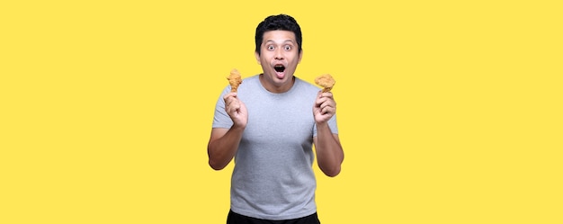 Hombre asiático está comiendo pollo frito deliciosamente sobre fondo amarillo
