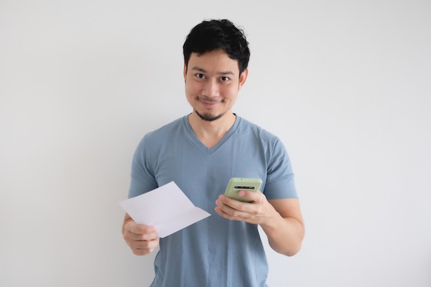 El hombre asiático está feliz por el teléfono inteligente y la factura en una pared aislada.