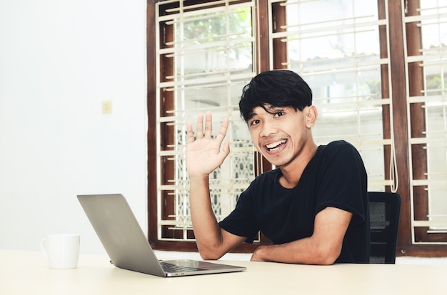 Un hombre asiático está sentado frente a la computadora portátil con una expresión sonriente
