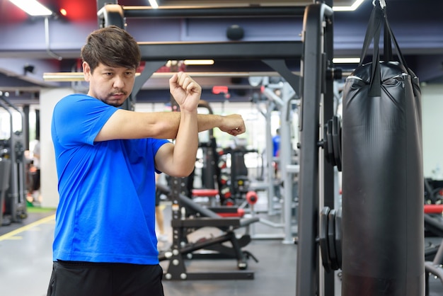 Hombre asiático estirando sus brazos en el gimnasio