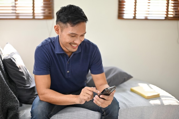 Hombre asiático feliz charlando con sus amigos en su teléfono mientras se relaja en su sala de estar