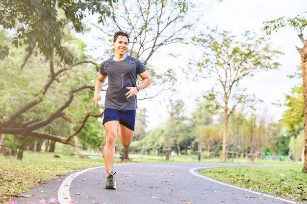 Hombre asiático feliz corriendo en el parque por la mañana