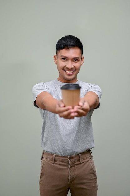 Hombre asiático feliz entregando una taza de café para llevar a la cámara aislada de fondo verde