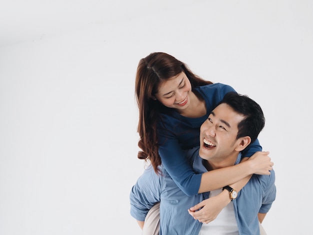 Hombre asiático feliz que lleva a su novia en la parte posterior sobre el fondo blanco, espacio de la copia.