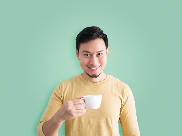 El hombre asiático feliz se refresca bebiendo y huele una taza de café.