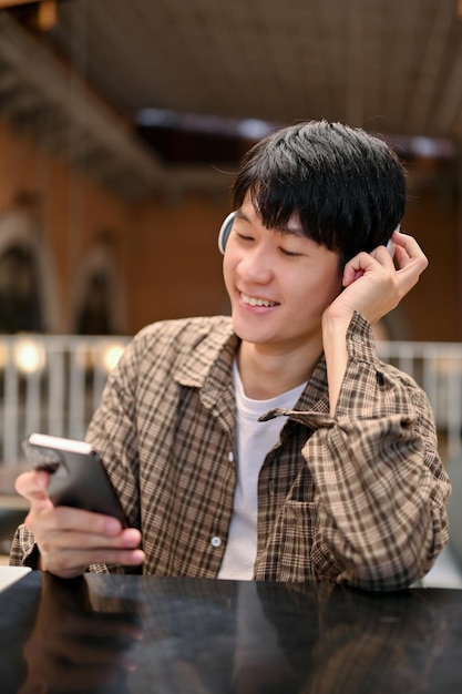 El hombre asiático feliz se sienta en el café escuchando música a través de sus auriculares