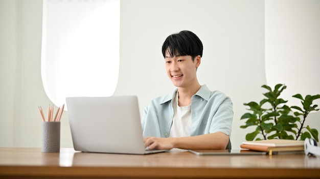 Hombre asiático feliz trabajando en sus tareas en la computadora portátil en su proyecto de gestión de trabajo de oficina mínimo