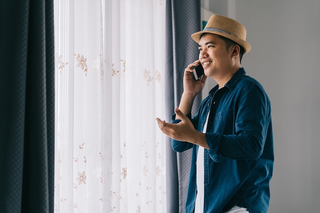 Hombre asiático felizmente realiza negocios a través del teléfono smar junto a la ventana.