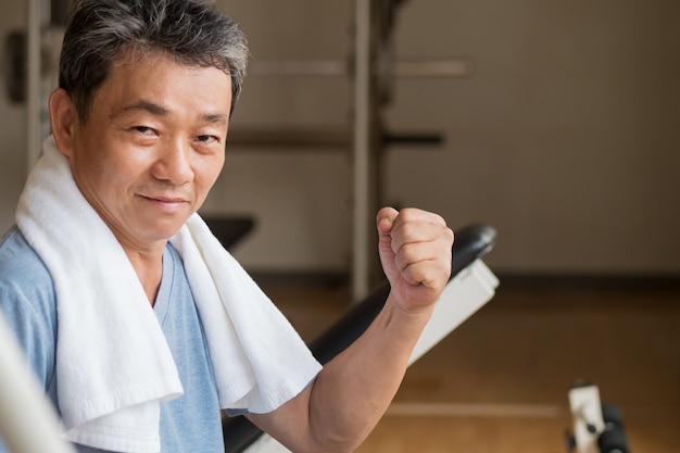 Hombre asiático fuerte, sano, feliz, sonriente, positivo del bienestar mayor que trabaja en el gimnasio