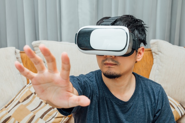 Hombre asiático con gafas de realidad virtual que expresan en el sofá marrón