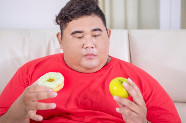 Hombre asiático gordo confundido entre manzana o donut