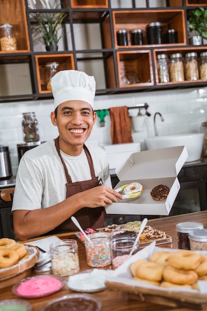 Hombre asiático con un gorro de cocinero mientras está sentado en la cocina