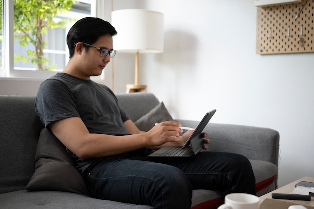 Hombre asiático guapo descansando en el sofá y navegando por internet con tableta de computadora.