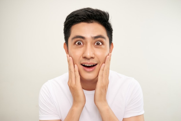 Foto hombre asiático guapo está tocando su rostro y sonriendo mientras se mira en el espejo