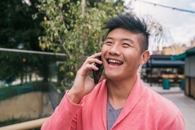 Hombre asiático hablando por teléfono al aire libre.