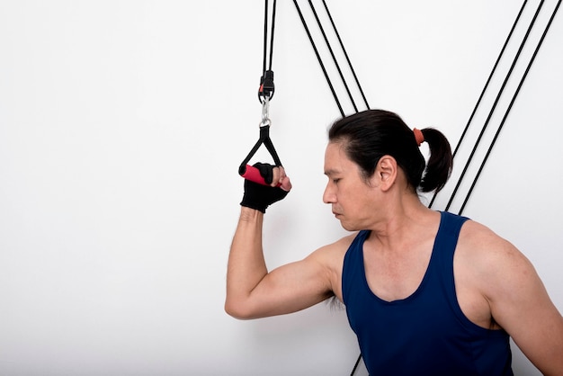 Hombre asiático haciendo ejercicio centrándose en tensar los músculos de la parte superior del brazo tirando de la cuerda