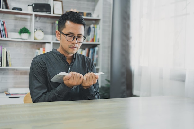 Hombre asiático haciendo las manos juntas en oración a Dios junto con la biblia En el concepto cristiano de la fe, la espiritualidad y la religión, los hombres oran en la biblia de oración de la biblia en la sala de estar en casa