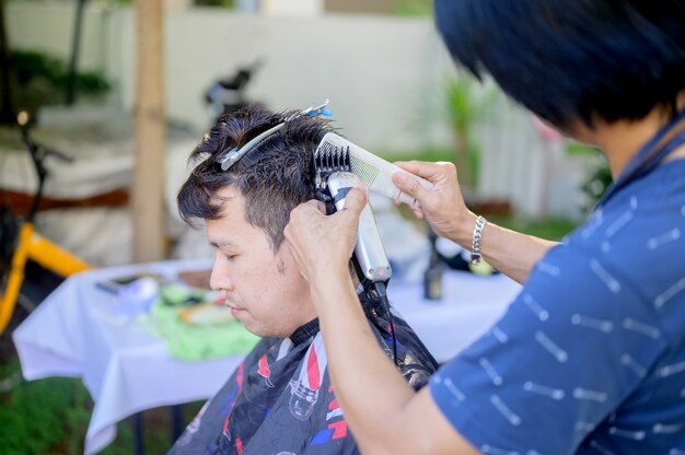 Hombre asiático haciendo negocios de peluquería y peluquería en casa. Peluquería al aire libre en el jardín. Distanciamiento social y nuevo estilo de vida normal.