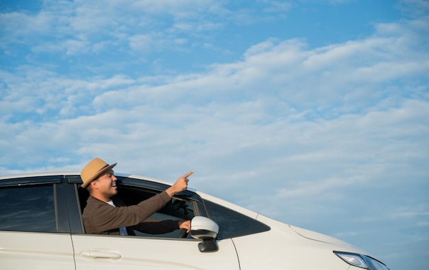 Hombre asiático hermoso joven que lleva el sombrero que conduce el coche ir a viajar en un cielo azul hermoso del día brillante.