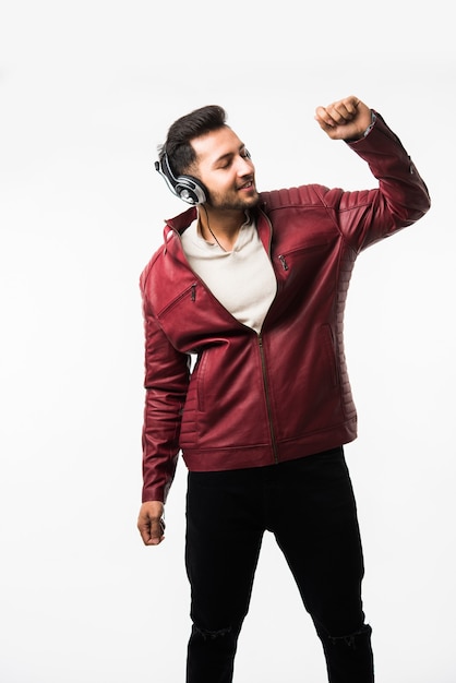 Hombre asiático indio con auriculares mientras llevaba chaqueta de cuero y bailando. aislado sobre fondo blanco