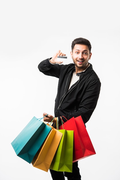 Hombre asiático indio mostrando sus bolsas de la compra y tarjeta de crédito o débito mientras está de pie sobre fondo blanco.