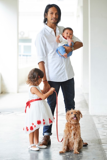 Hombre asiático joven elegante hermoso que camina con su pequeño hijo, hija y perro lindo con correa