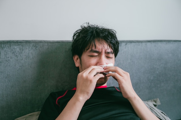 El hombre asiático joven está usando la servilleta para limpiar la mucosidad de su nariz de enfermedad.