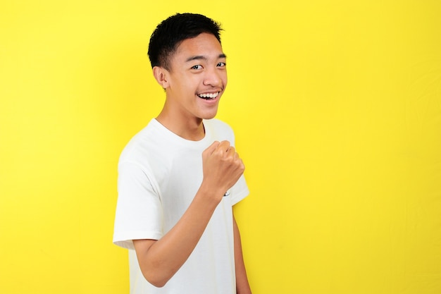 Hombre asiático joven feliz y emocionado expresando gesto ganador. Exitoso y celebrando sobre fondo amarillo