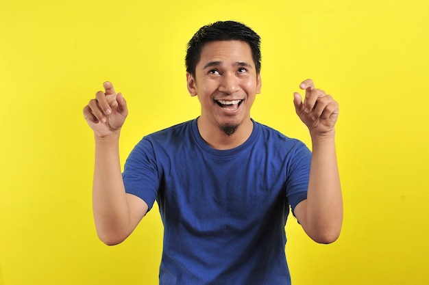 Hombre asiático joven feliz y emocionado expresando gesto ganador. Exitoso y celebrando sobre fondo amarillo