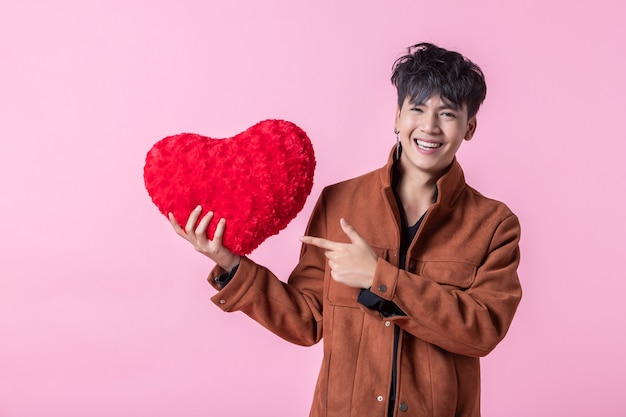 Un hombre asiático joven guapo sosteniendo una almohada en forma de corazón rojo