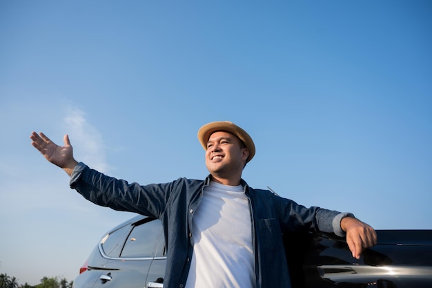 Hombre asiático joven hermoso que consigue el coche nuevo. Él de pie delante del coche. Él muy feliz. Concepto de compra o alquiler de coche.