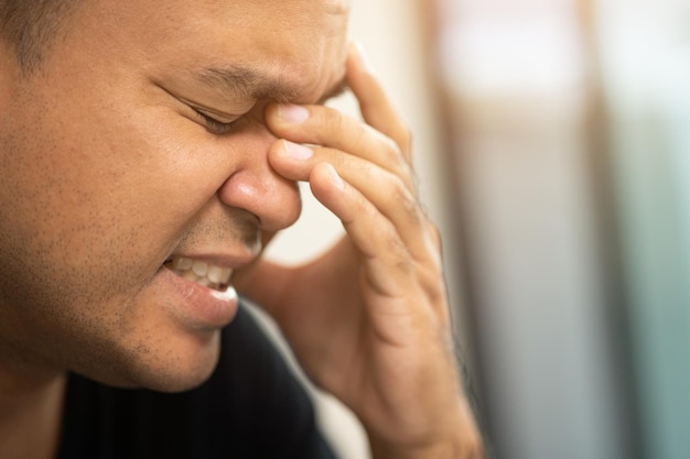 Hombre asiático joven con la mano en la cabeza que se siente deprimido, estrés, dolor de cabeza cansado de trabajar mucho tiempo con el síndrome de la oficina de síntomas.