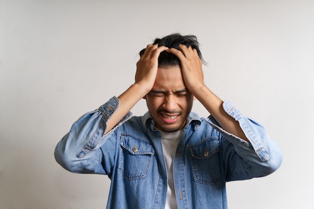 El hombre asiático joven puso las manos a su cabeza. Se siente enfermo y con dolor de cabeza por tener algunos problemas.