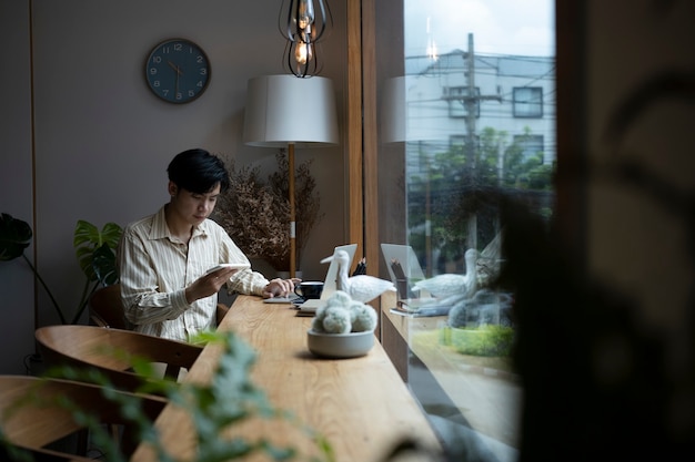 Hombre asiático joven que se sienta en la cafetería y que usa el teléfono inteligente.