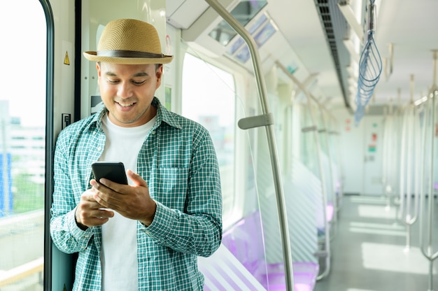 Hombre asiático joven que sonríe usando smartphone en metro o tren de cielo