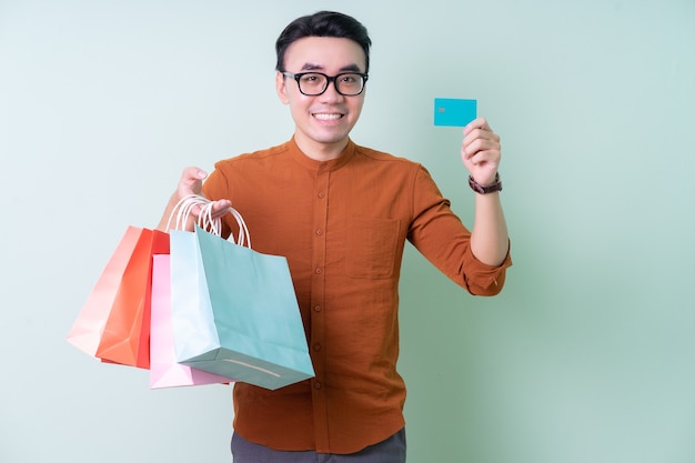 Hombre asiático joven que sostiene el bolso de compras en fondo verde