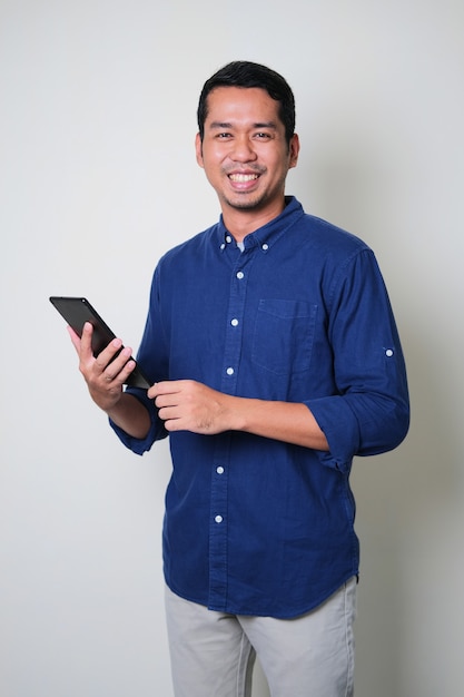 Hombre asiático joven que sostiene el gadget de la tableta móvil mientras sonríe confiado