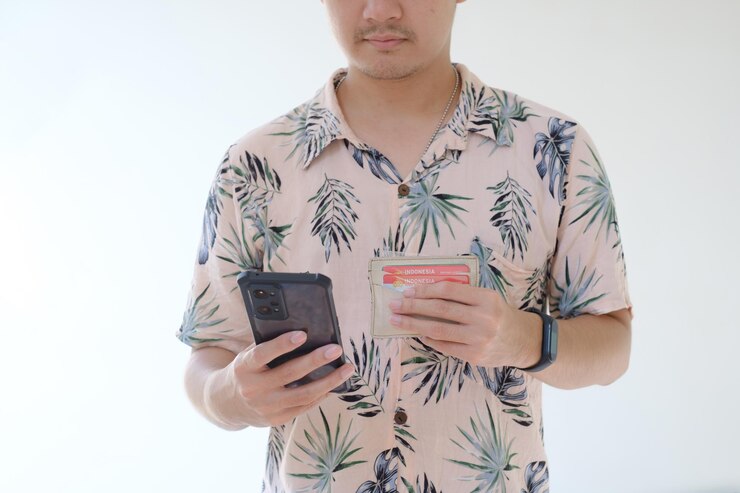 Hombre asiático joven que sostiene un teléfono inteligente y una billetera que contiene licencias de conducir de Indonesia