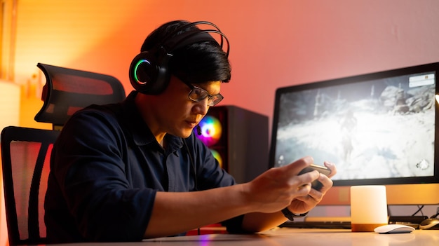 Hombre asiático jugando en el teléfono móvil Jugador profesional jugando videojuegos en una computadora personal Sala de luces de neón coloridas Juego en línea Esport